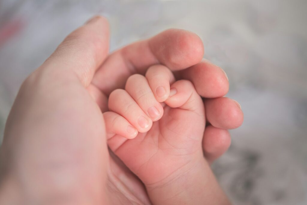 Main d’un adulte tenant la main d’un bébé, image d’illustration pour un article sur les allocations familiales.